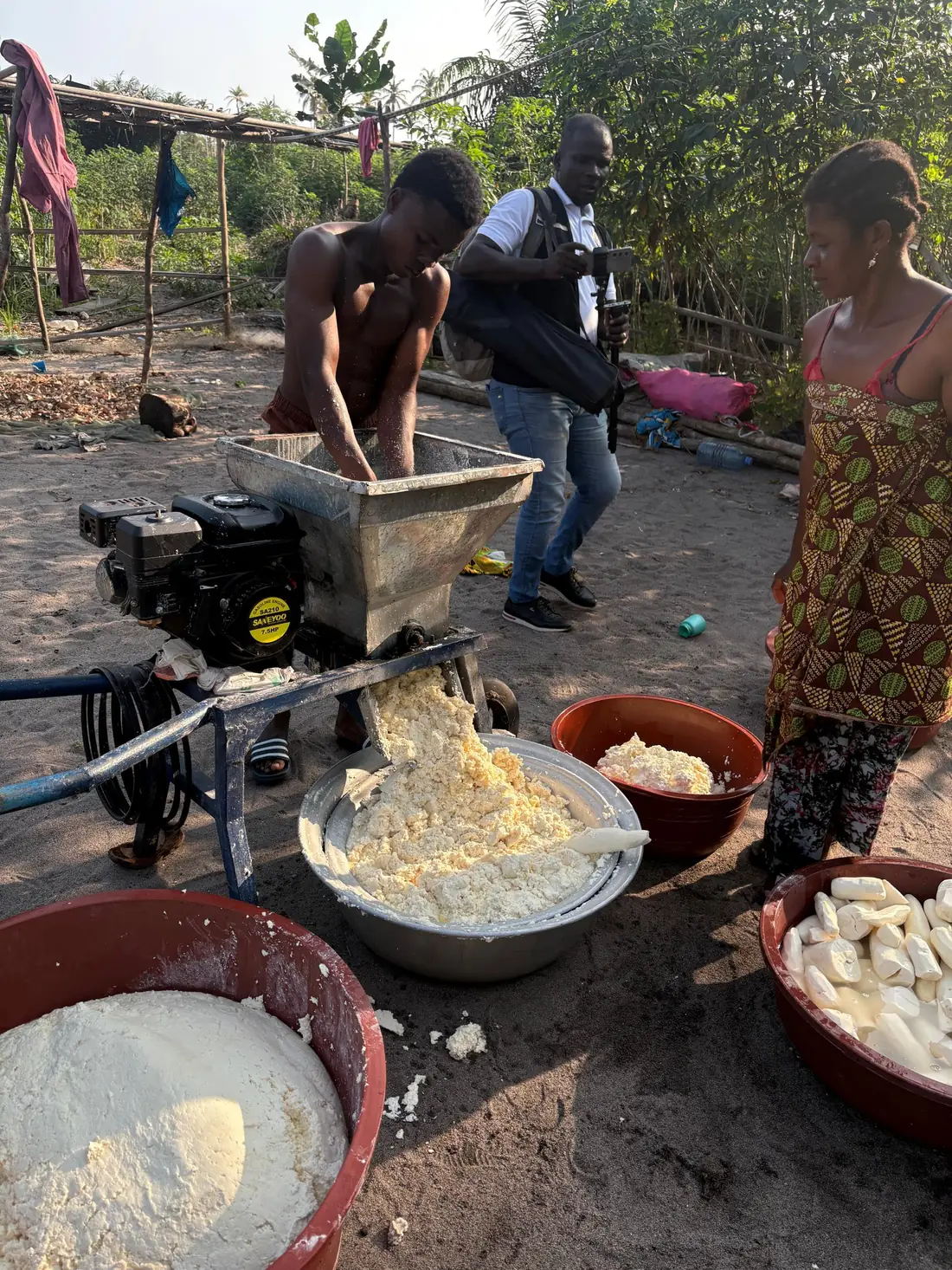 Broyage du manioc à l'aide d'une machine, avec l'équipe de tournage sur place, à Dibou